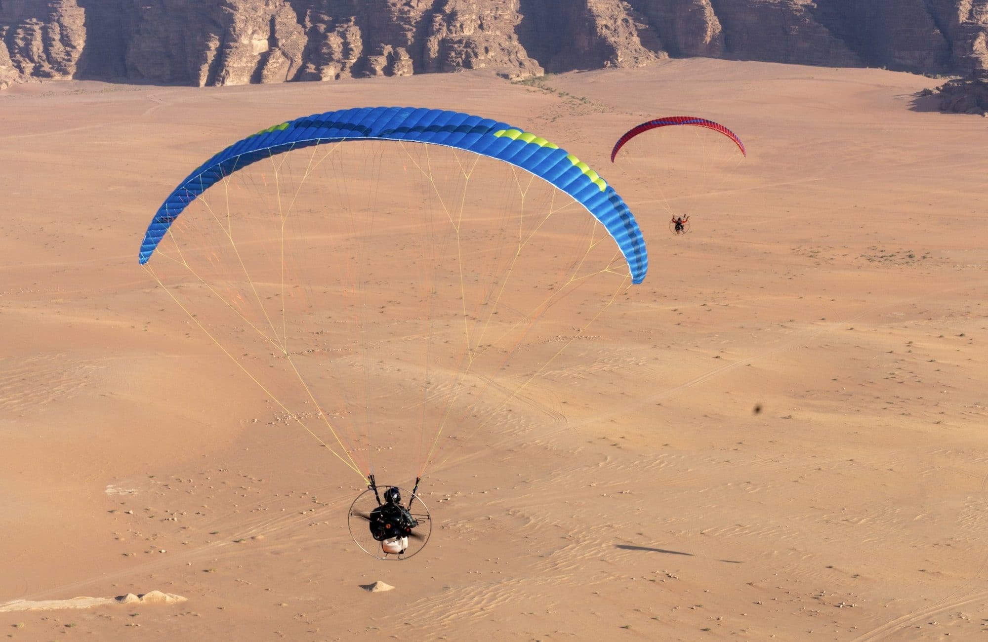 Pilots kiting paramotor wings in sand dunes